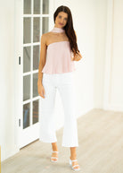 Woman wearing a light pink strapless top and white pants indoors.