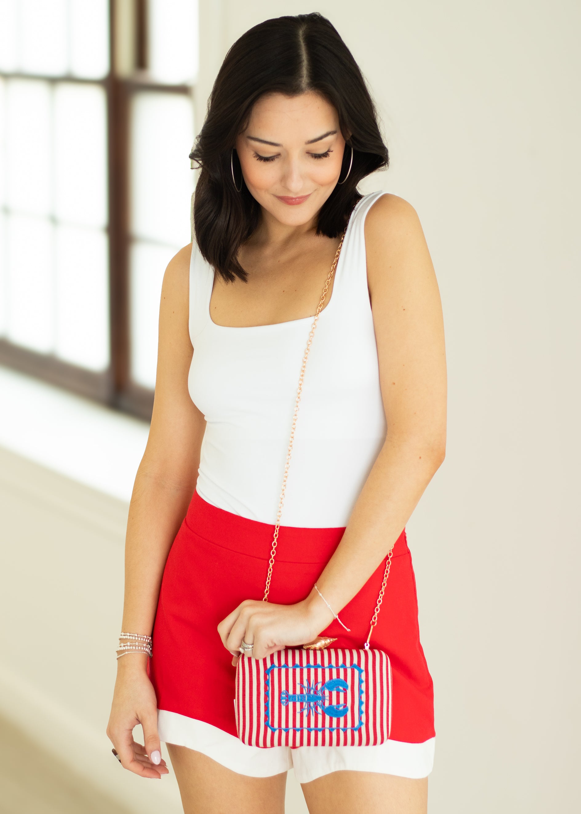 Woman holding a small handbag with a design, wearing a white top and red skirt.