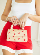 Person holding a small woven clutch with red lobster patterns, wearing a white top and red shorts.