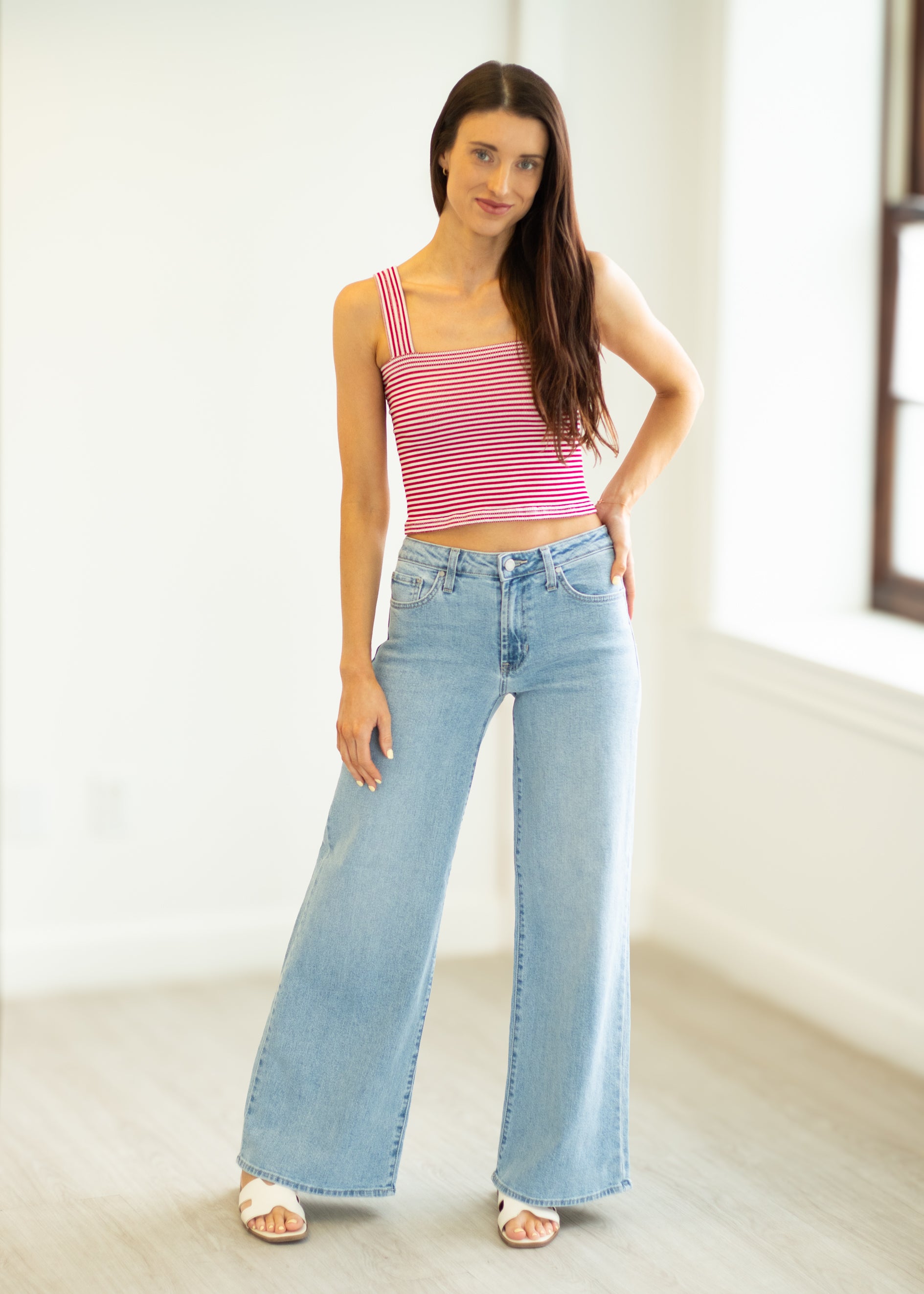 Woman wearing a pink striped top and light blue jeans in a bright room.