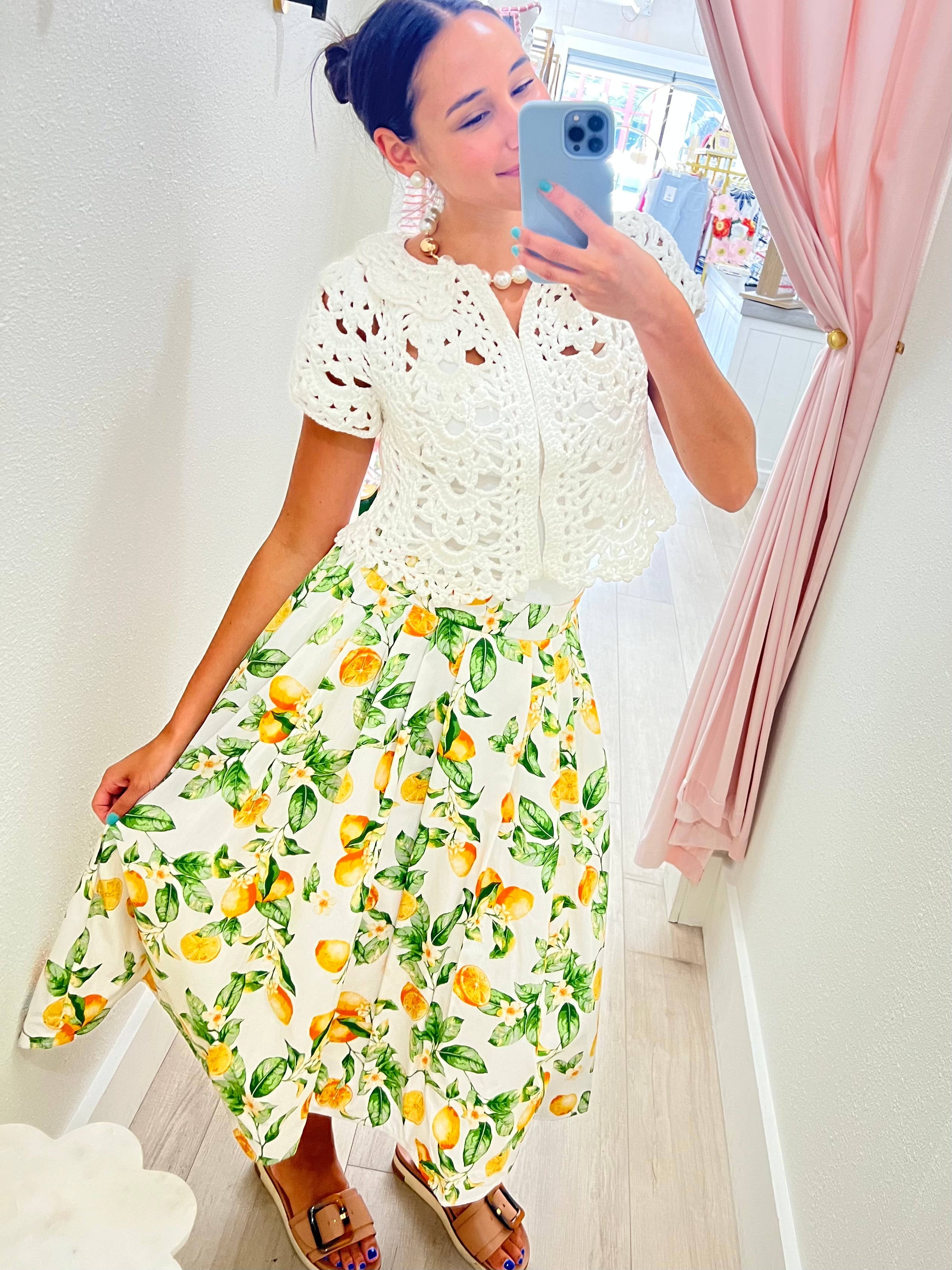Woman taking a mirror selfie wearing a white lace top and floral skirt.