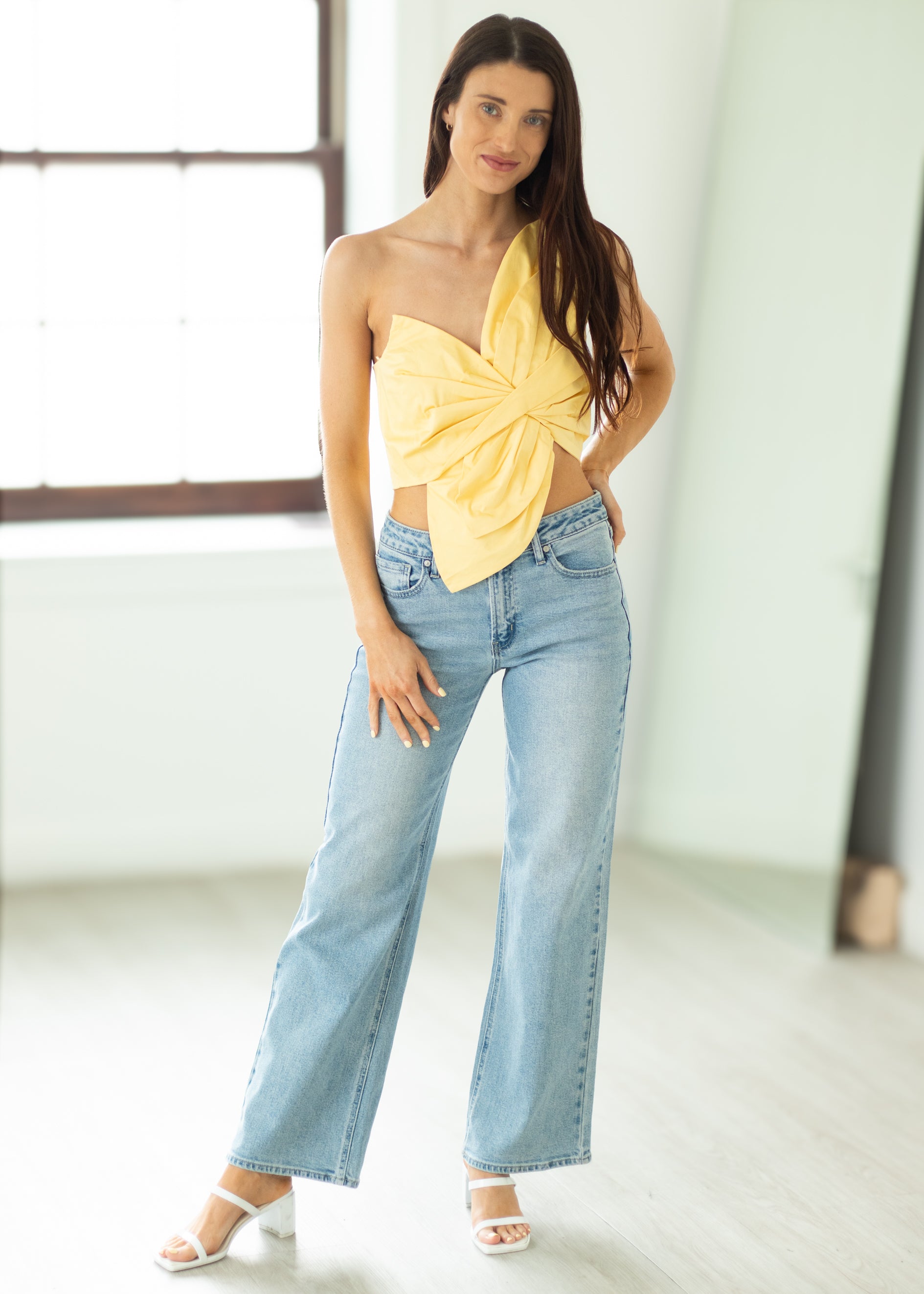 Woman wearing a yellow strapless top and blue jeans indoors.