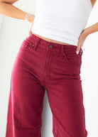 A close-up of a person wearing high-waisted, wide-leg red denim jeans with a white sleeveless top, standing against a plain white background.