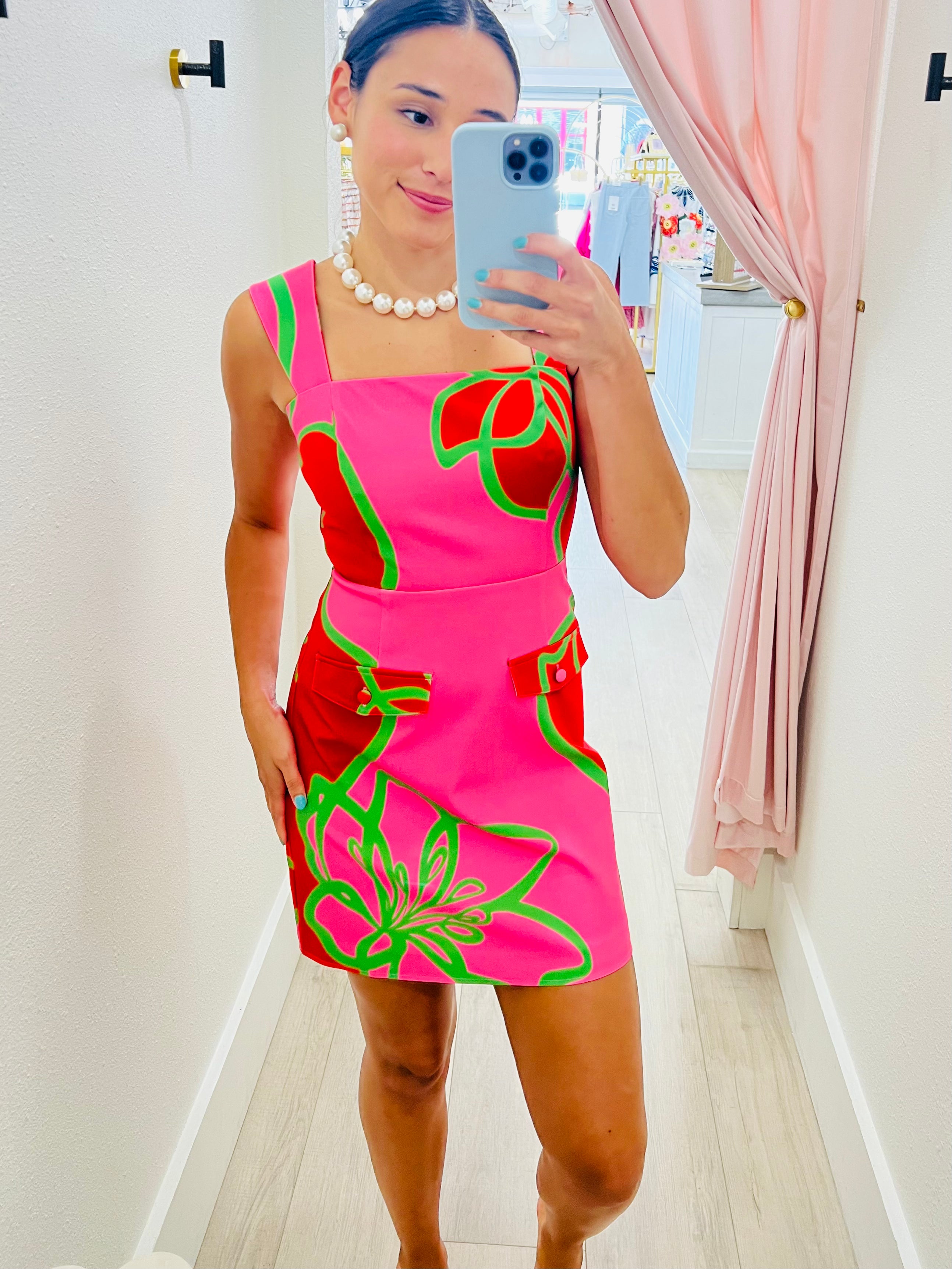 Woman taking a mirror selfie wearing a pink dress with red and green floral patterns.
