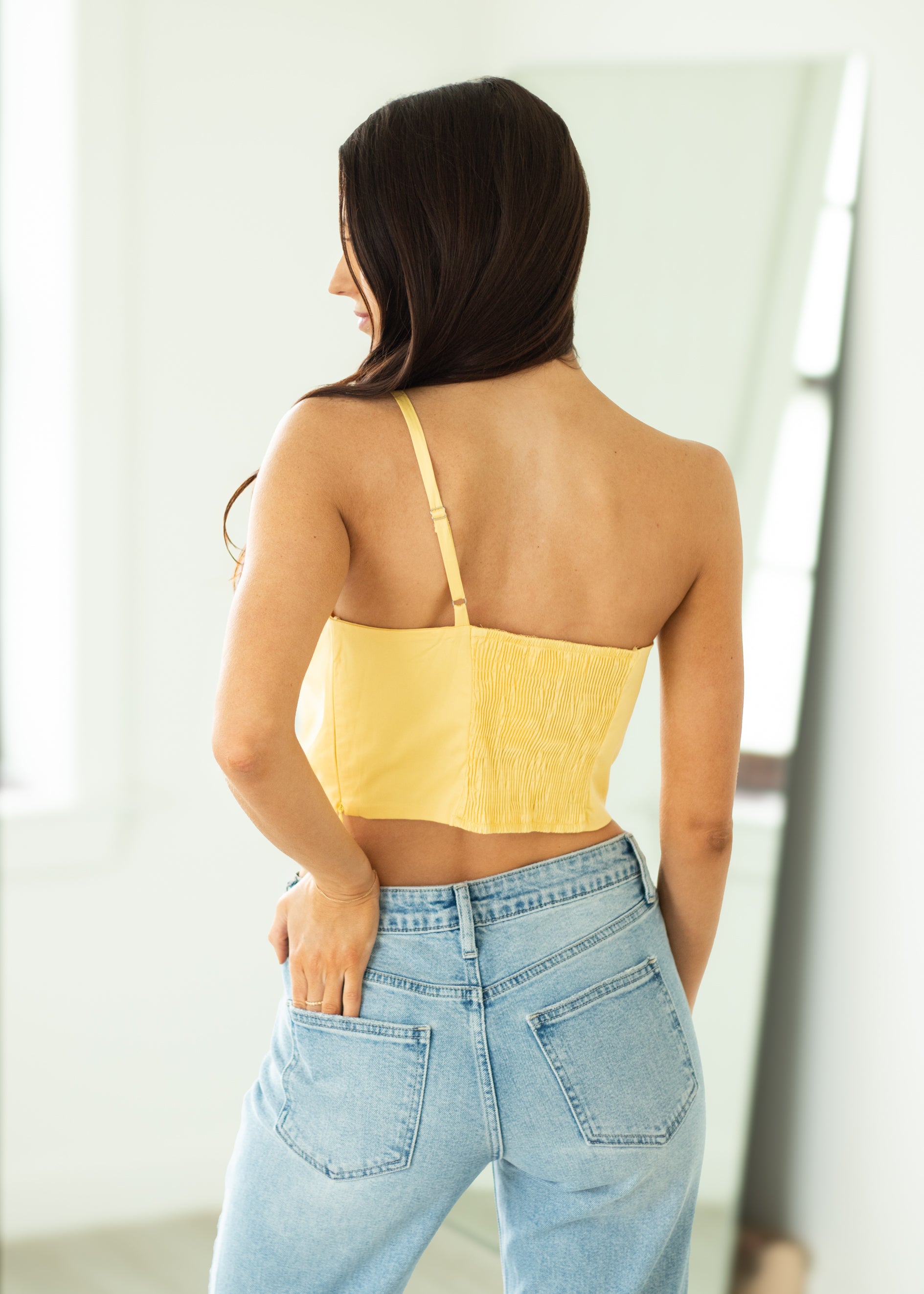 Woman wearing a yellow top and blue jeans against a white wall