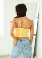 Woman wearing a yellow top and blue jeans against a white wall