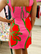 Person wearing a bright pink dress with red floral patterns in a clothing store.