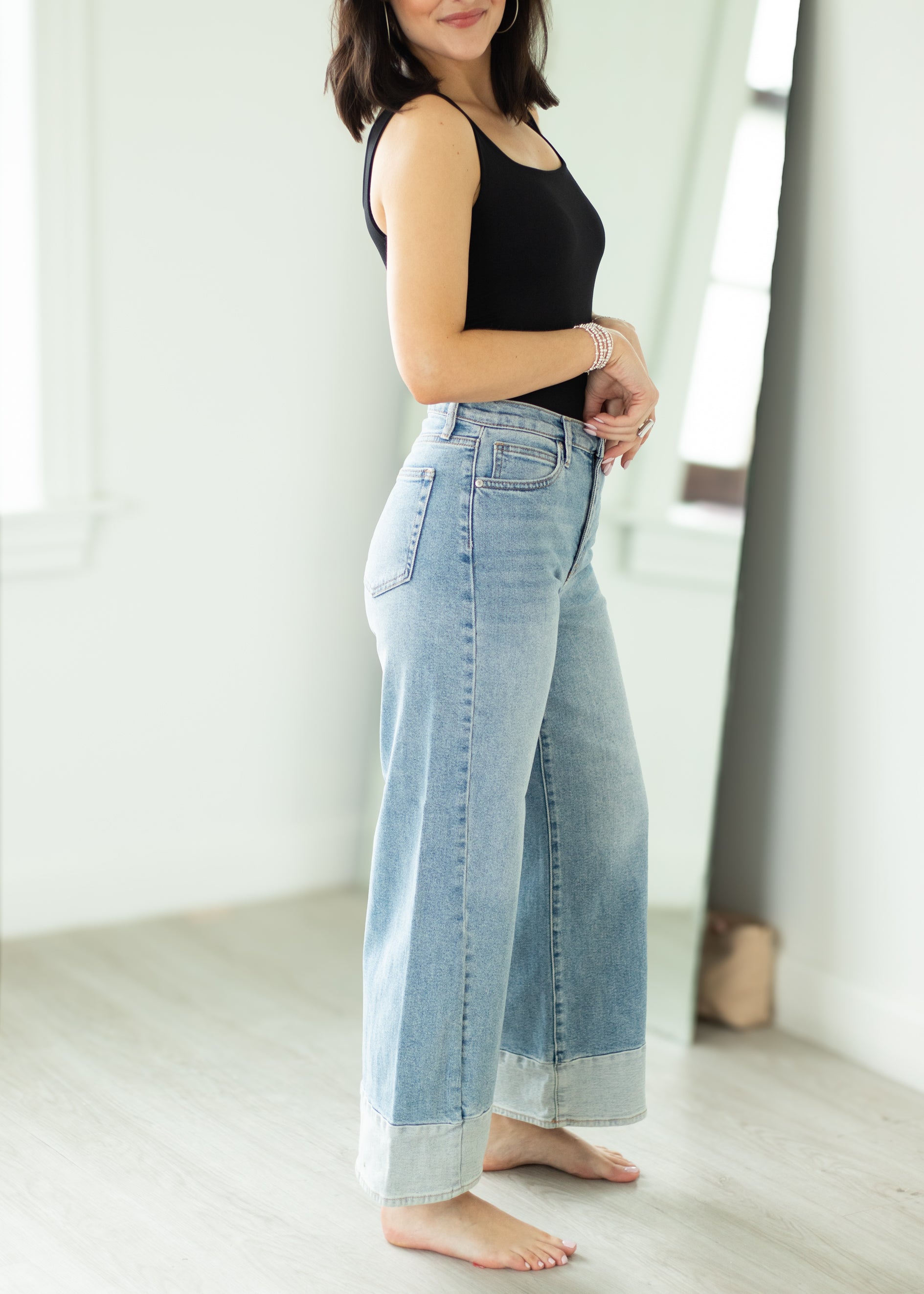 Woman wearing light blue jeans and a black top in a bright room.