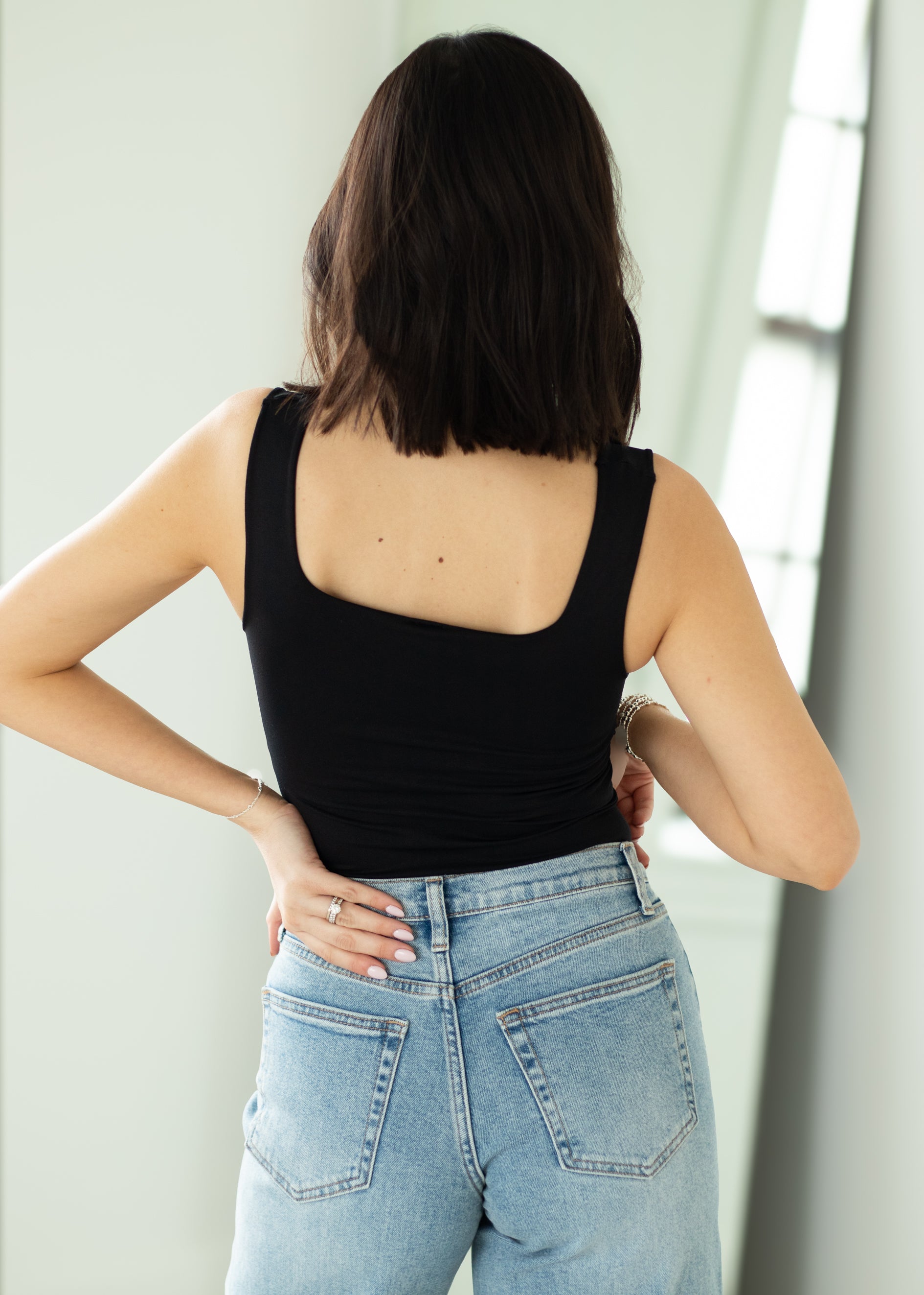 Person wearing a black tank top and light blue jeans against a white wall.