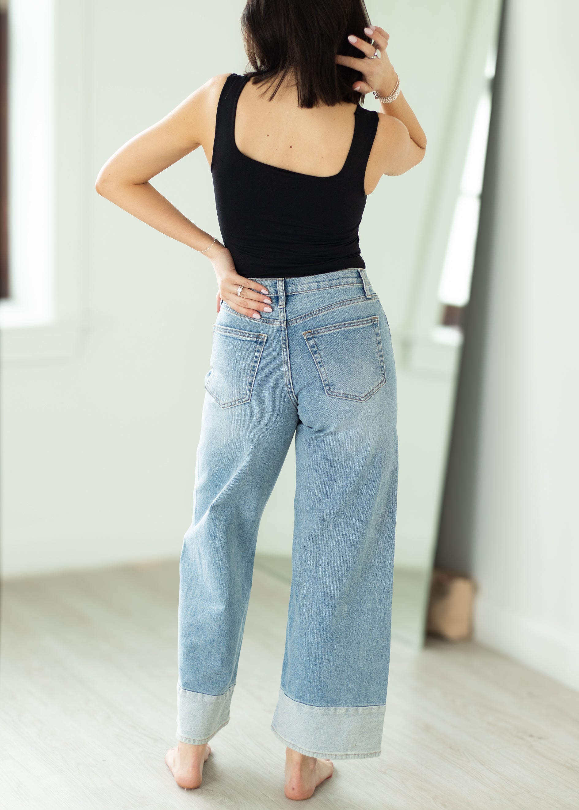 Person wearing a black tank top and light blue jeans indoors.