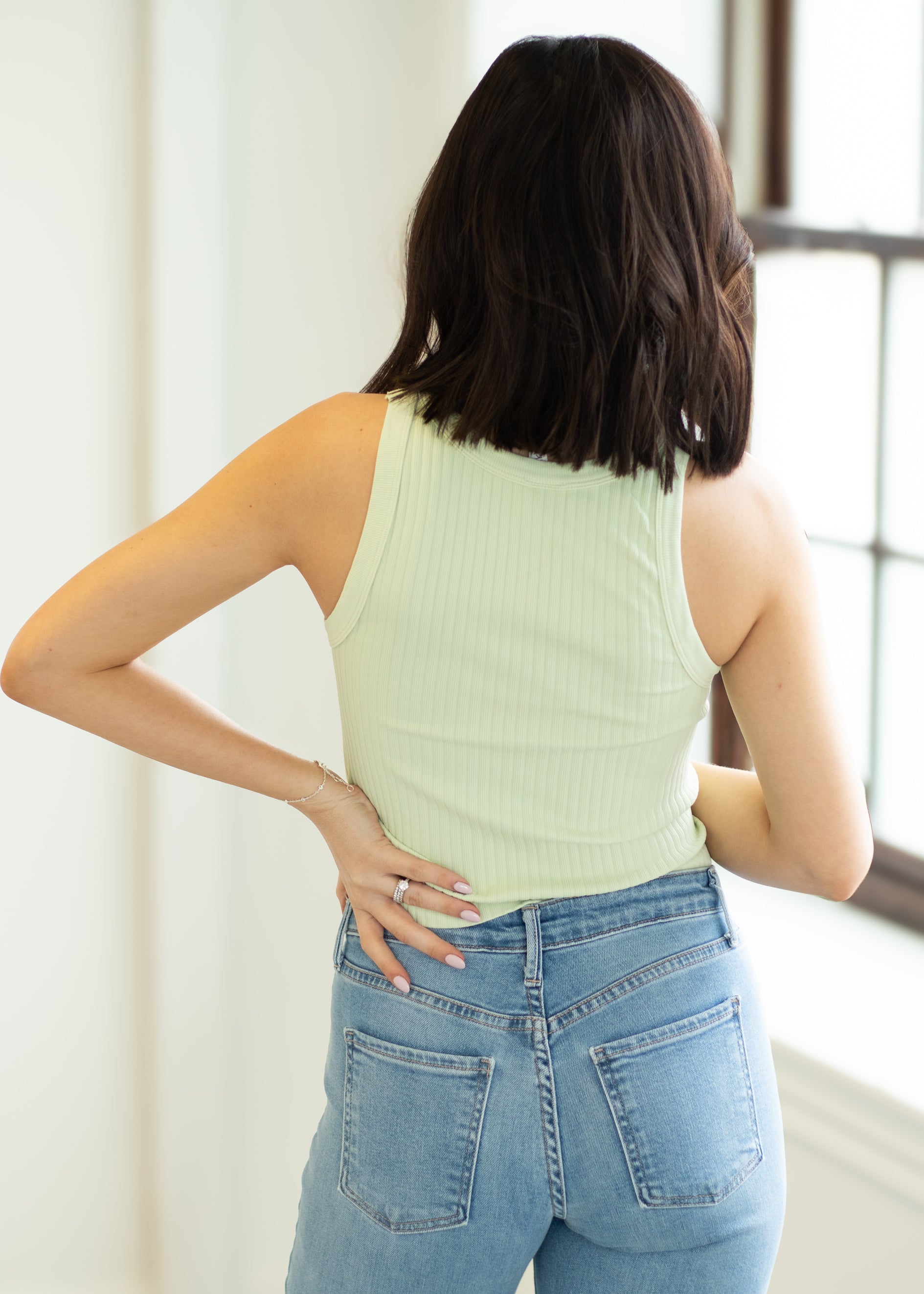 Woman wearing a light green sleeveless top and blue jeans, standing indoors.