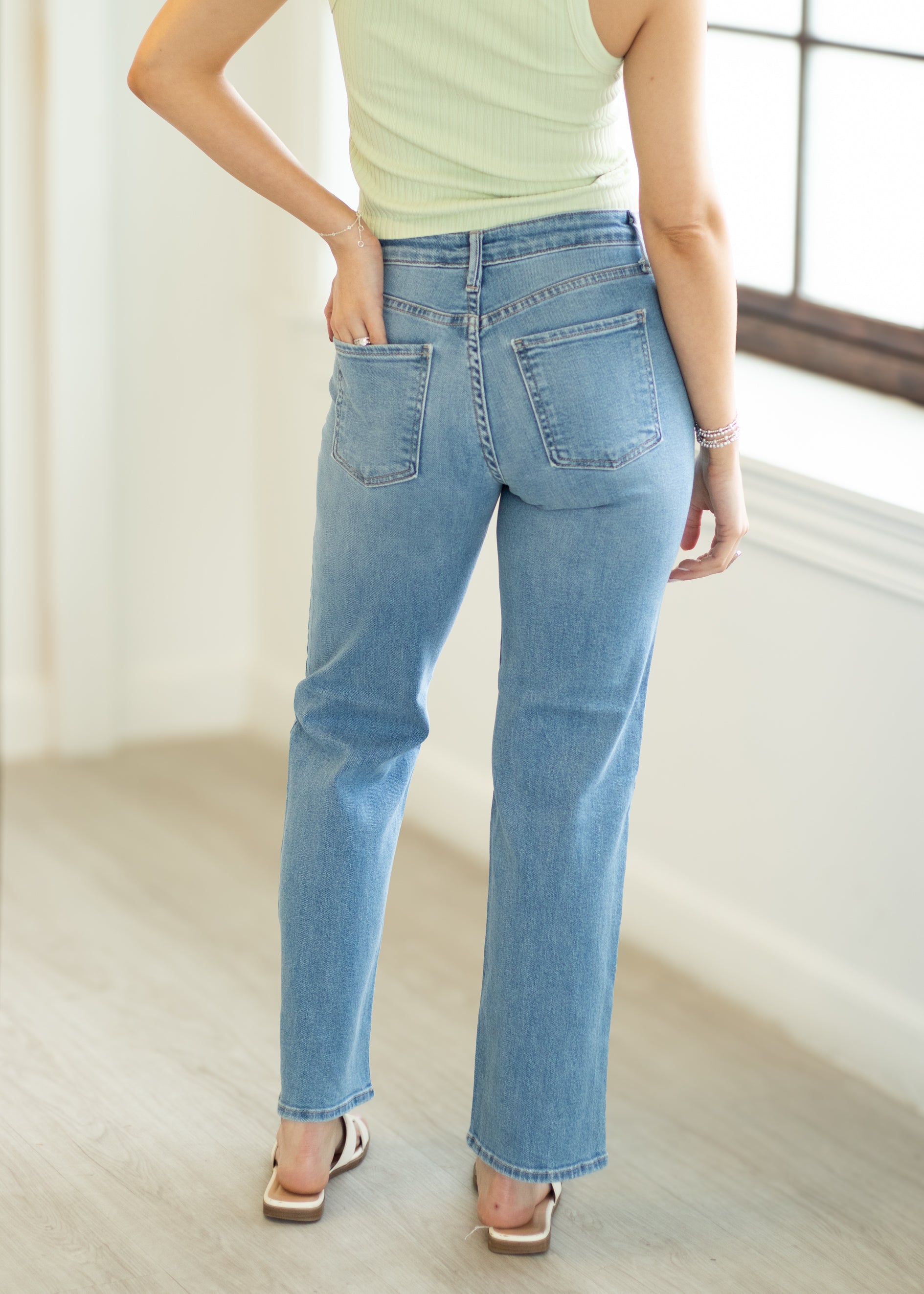 Person wearing light blue jeans and a light green top in a bright room.