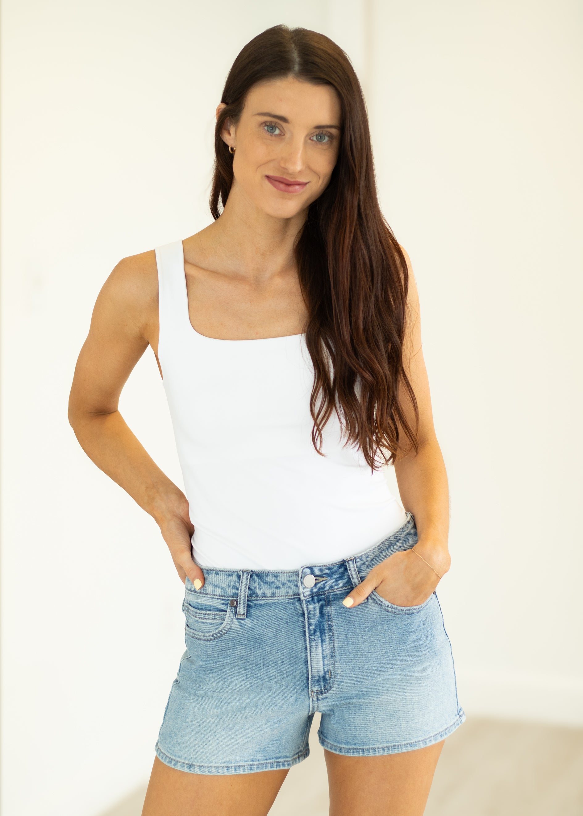 Woman wearing a white tank top and denim shorts on a plain background