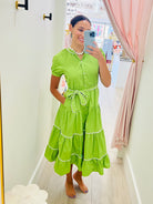 Woman taking a mirror selfie wearing a green dress with white trim.