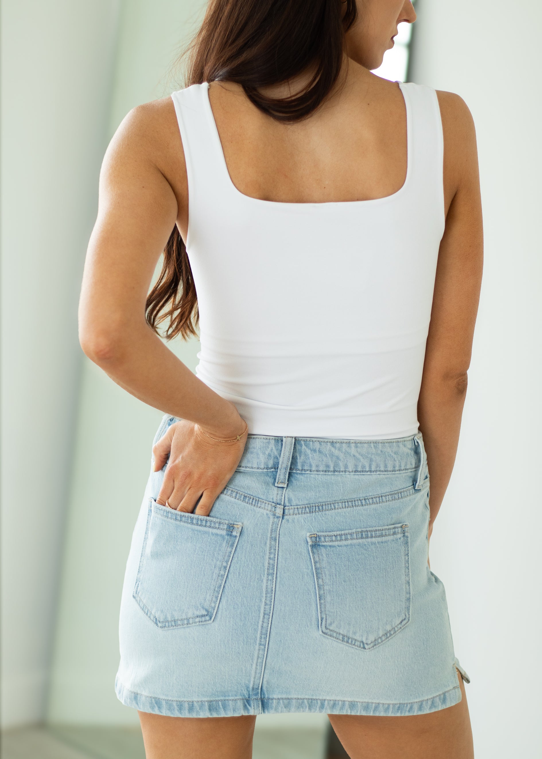 Woman wearing a white tank top and light blue denim skirt against a neutral background