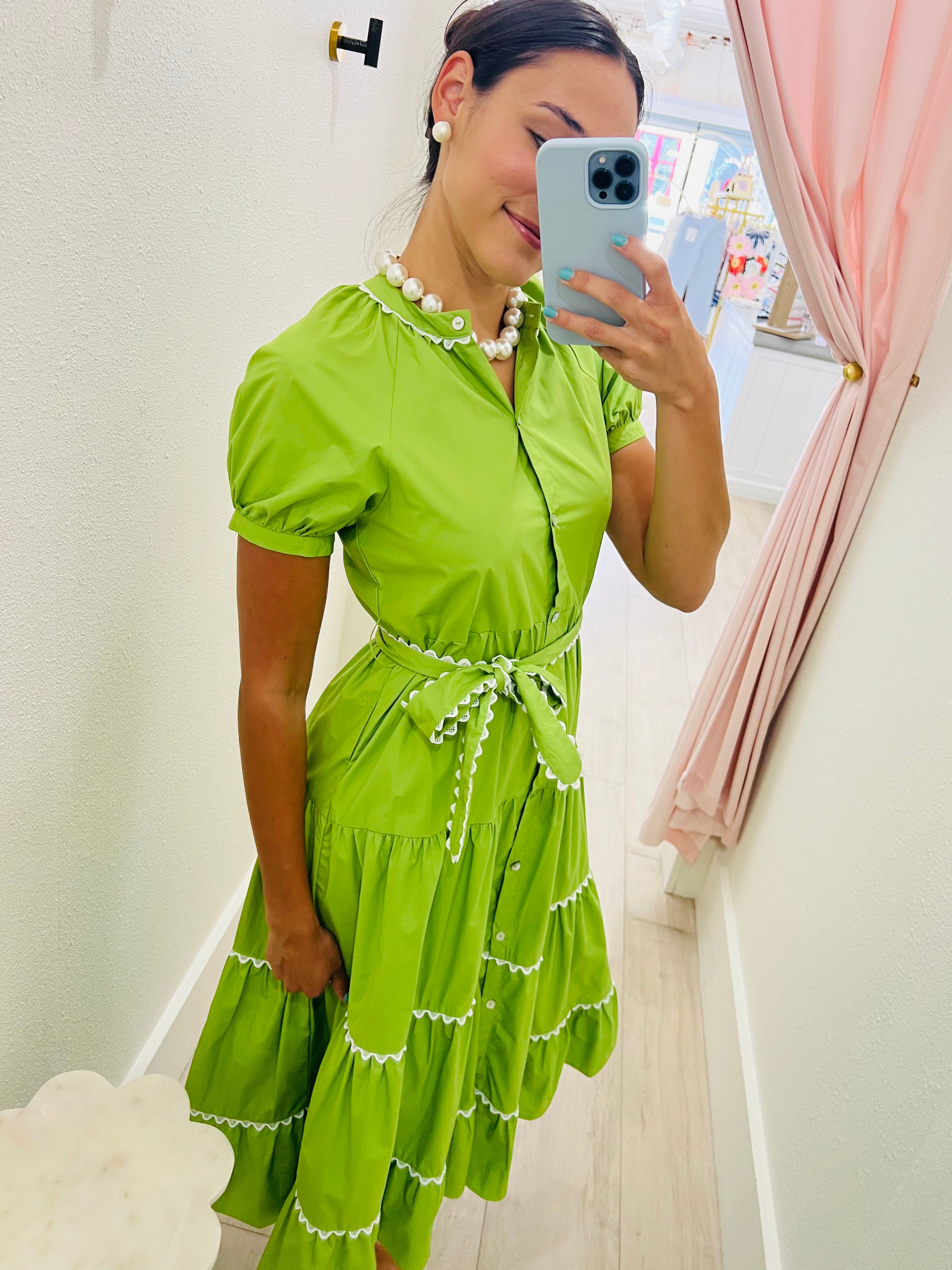 Woman taking a mirror selfie wearing a green dress with white trim.
