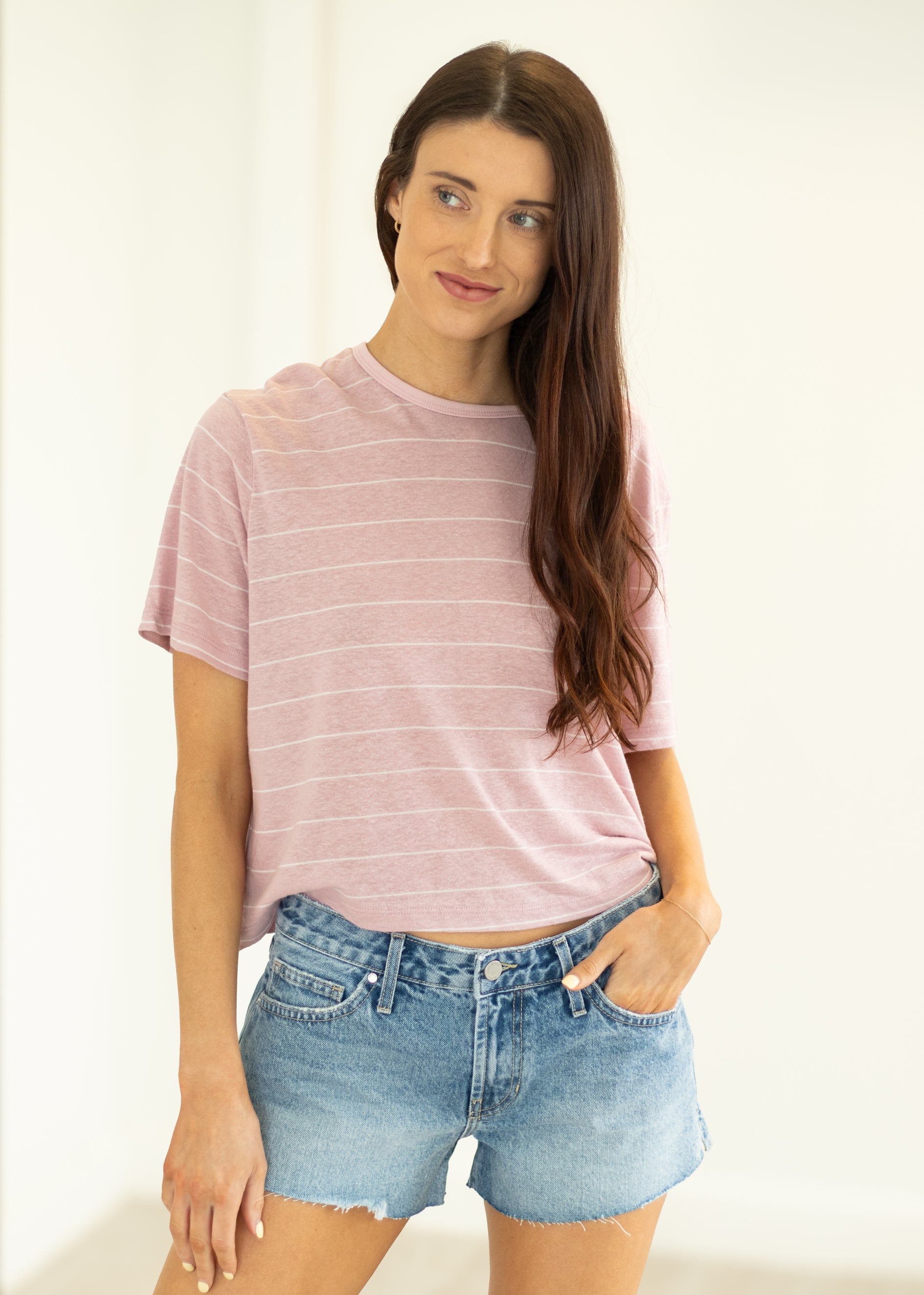 Woman wearing a pink striped t-shirt and denim shorts against a white background