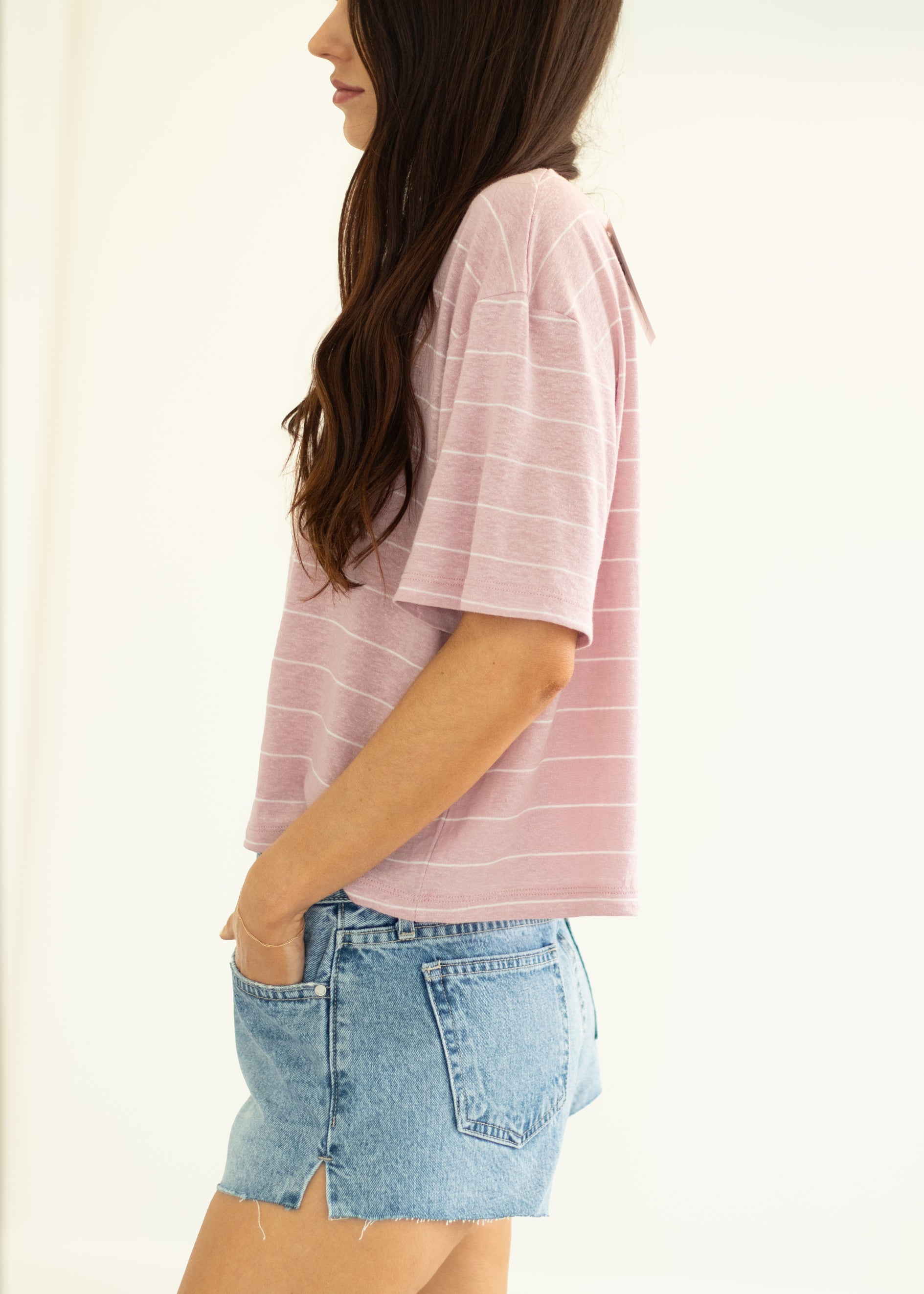 Woman wearing a pink striped shirt and denim shorts on a plain background