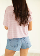 Person wearing a pink striped shirt and denim shorts on a plain background