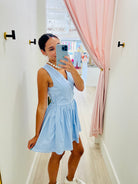 Woman taking a mirror selfie wearing a light blue dress in a room with pink curtains.