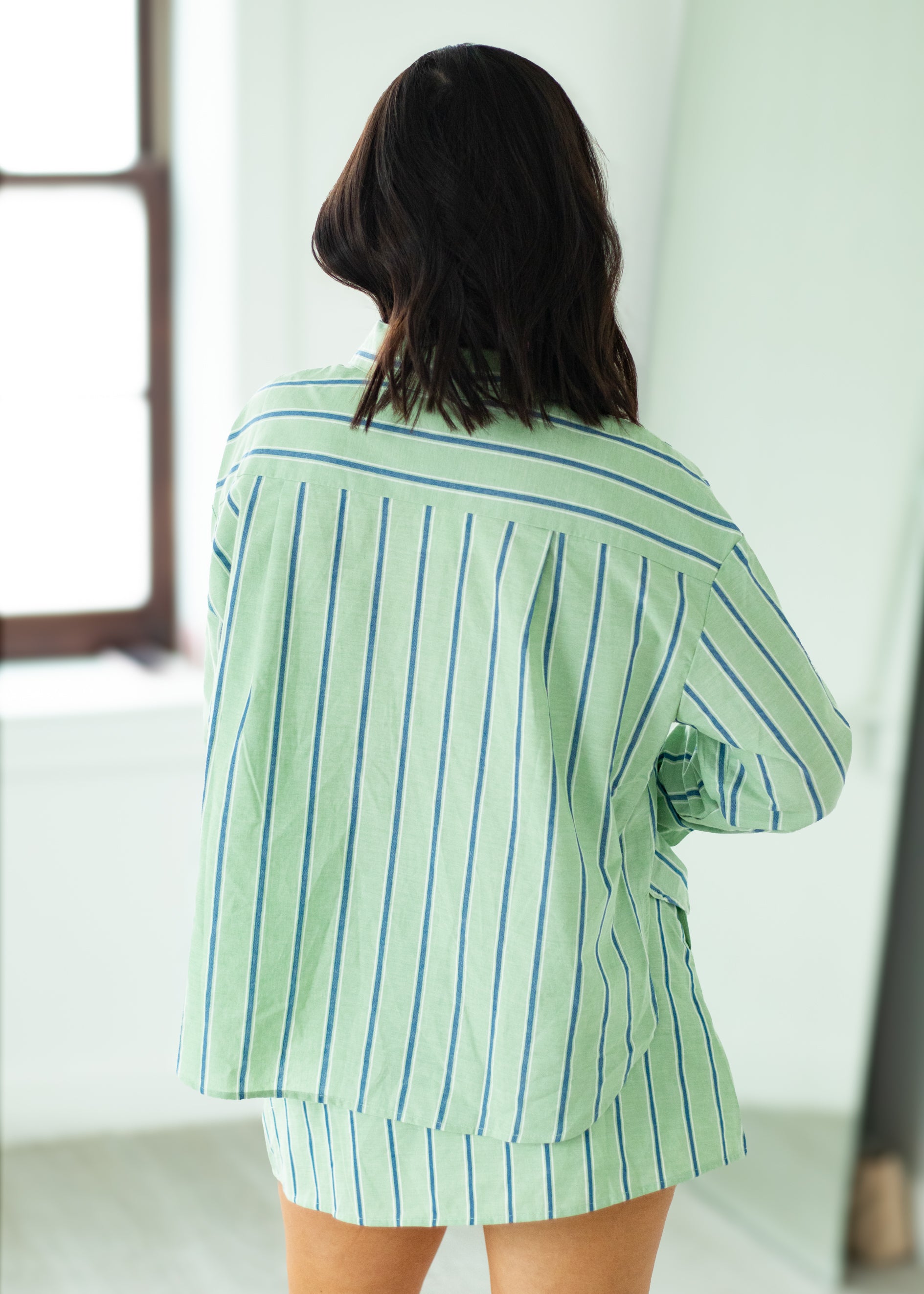 Woman wearing a green and white striped shirt and skirt in a bright room.