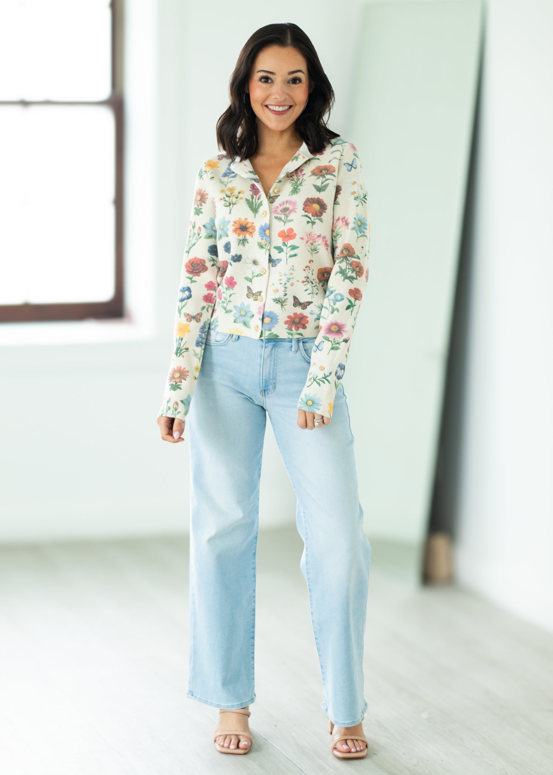 Woman wearing a floral blouse and light blue jeans in a bright room.
