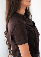 A woman shown in side profile wearing a dark brown short-sleeve knit cowl-neck top against a plain light background.
