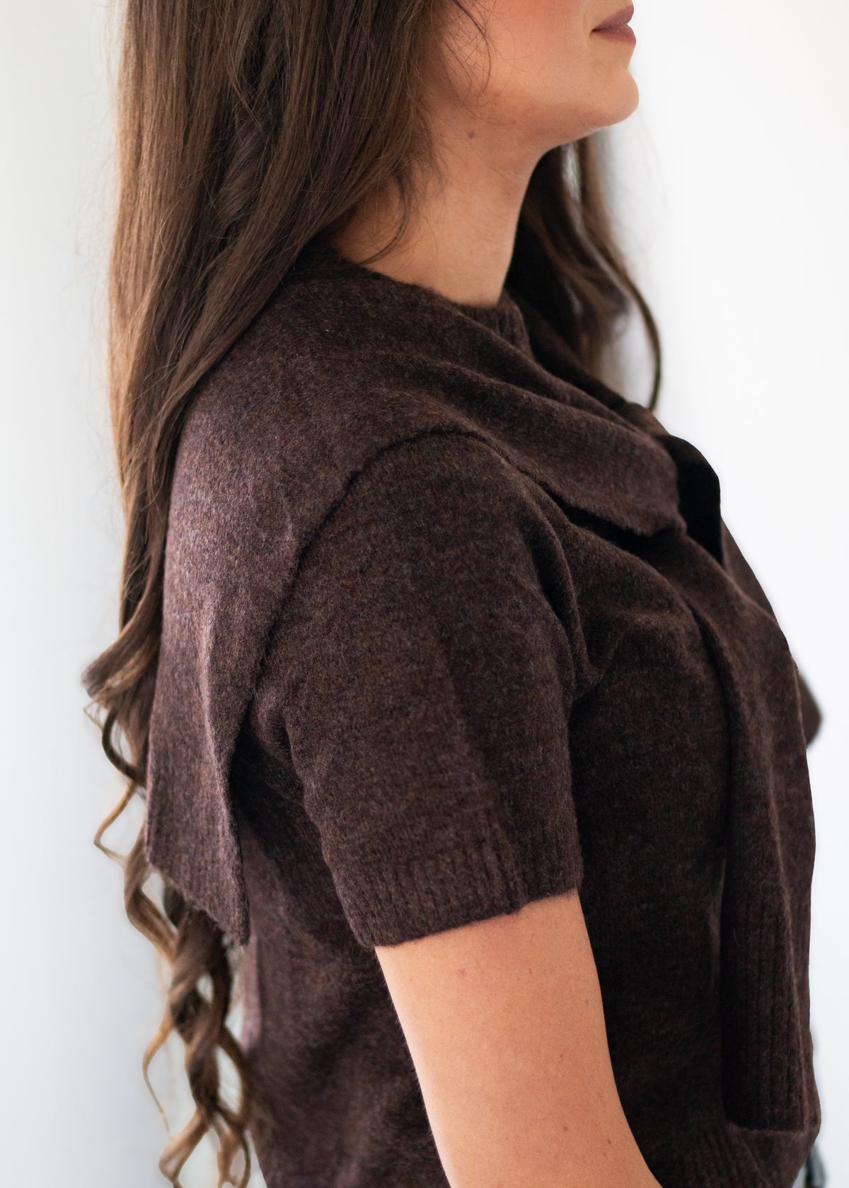 A woman shown in side profile wearing a dark brown short-sleeve knit cowl-neck top against a plain light background.