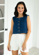 Woman wearing a denim vest over a white top and shorts indoors.