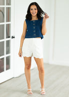 Woman wearing a denim vest over a white top and shorts indoors.