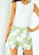Person wearing a white sleeveless top and floral shorts against a light background