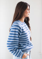 A woman in side profile wearing a blue and white striped knit sweater, paired with light blue jeans, against a plain white background.