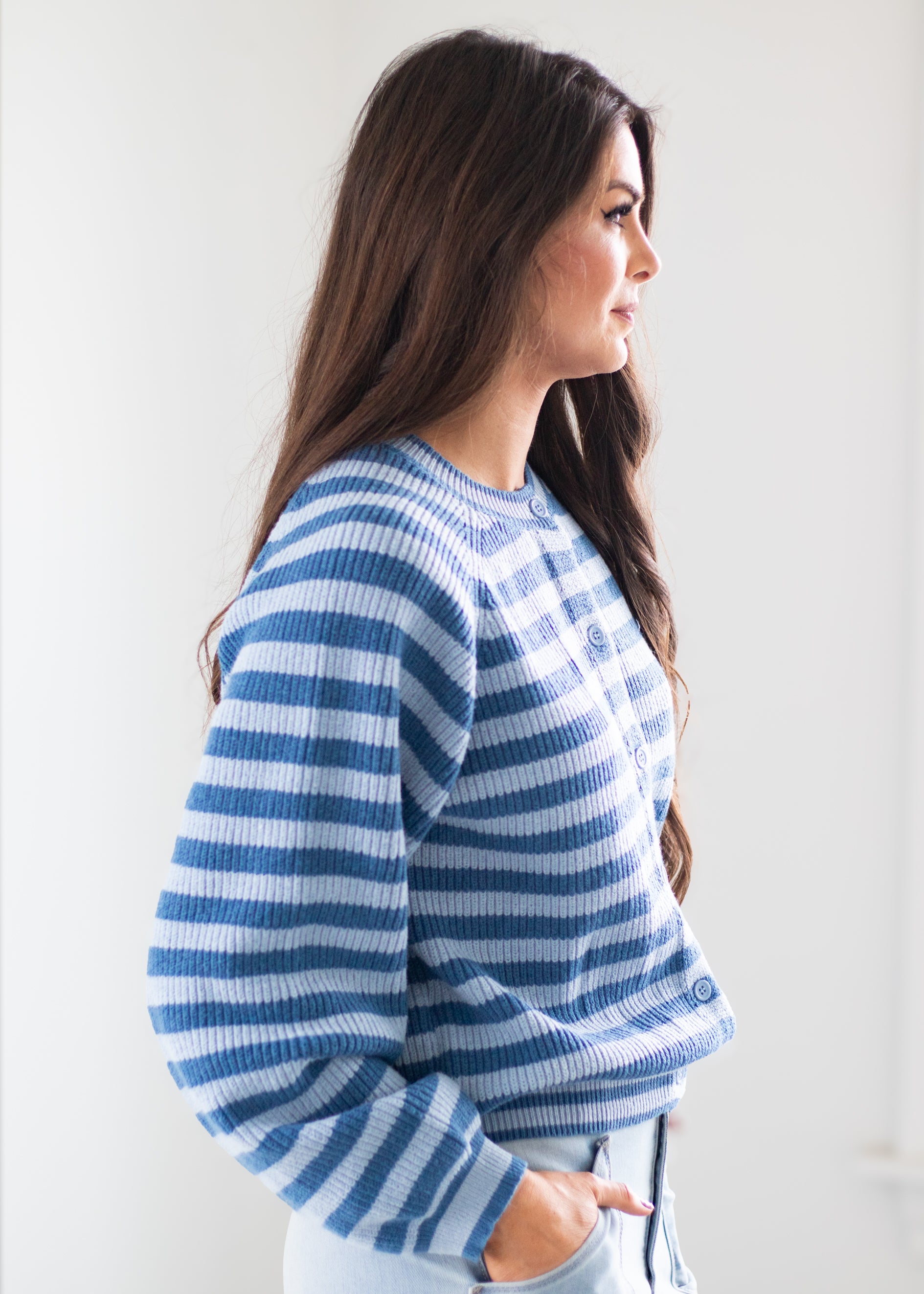 A woman in side profile wearing a blue and white striped knit sweater, paired with light blue jeans, against a plain white background.