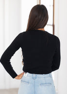A woman shown from behind wearing a fitted black long-sleeve top and light blue jeans in a bright indoor setting.