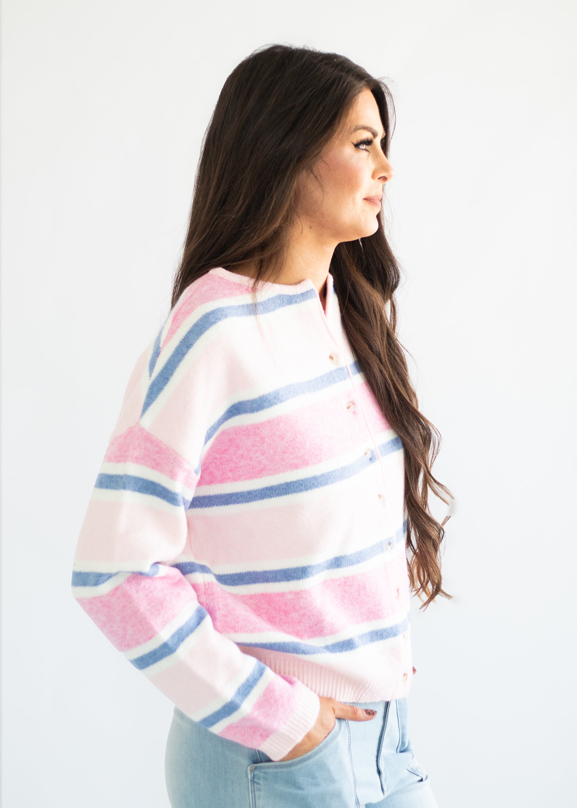 A woman wearing a fuzzy knit sweater with horizontal pink, white, and blue stripes, paired with light blue jeans, shown from a side profile against a plain white background.