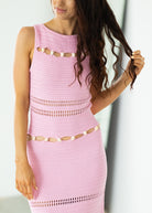 Woman wearing a pink crochet dress with cut-out details against a white background