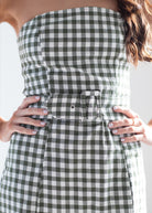 A close-up of a woman wearing a strapless green and white gingham dress with a matching belt and large buckle at the waist.
