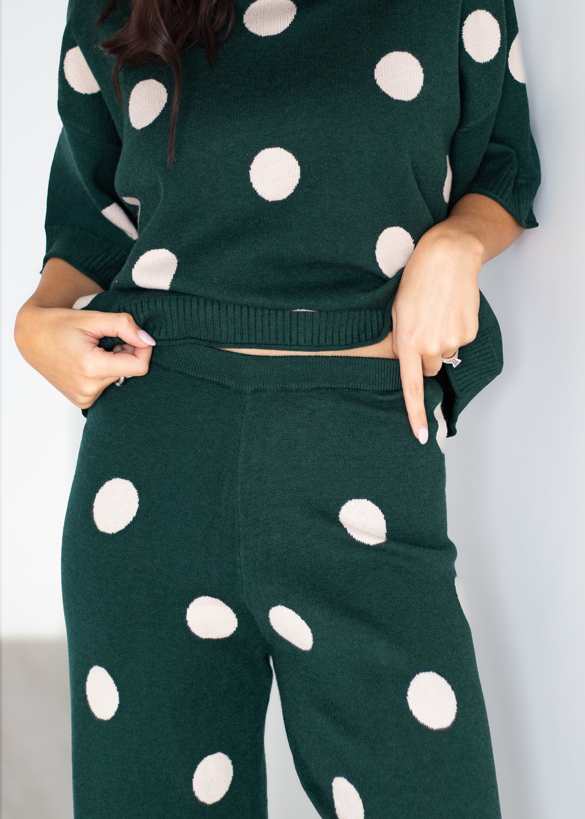 A person wearing a dark green knit matching set with large white polka dots, including a cropped sweater and wide-leg pants, shown against a plain light background.