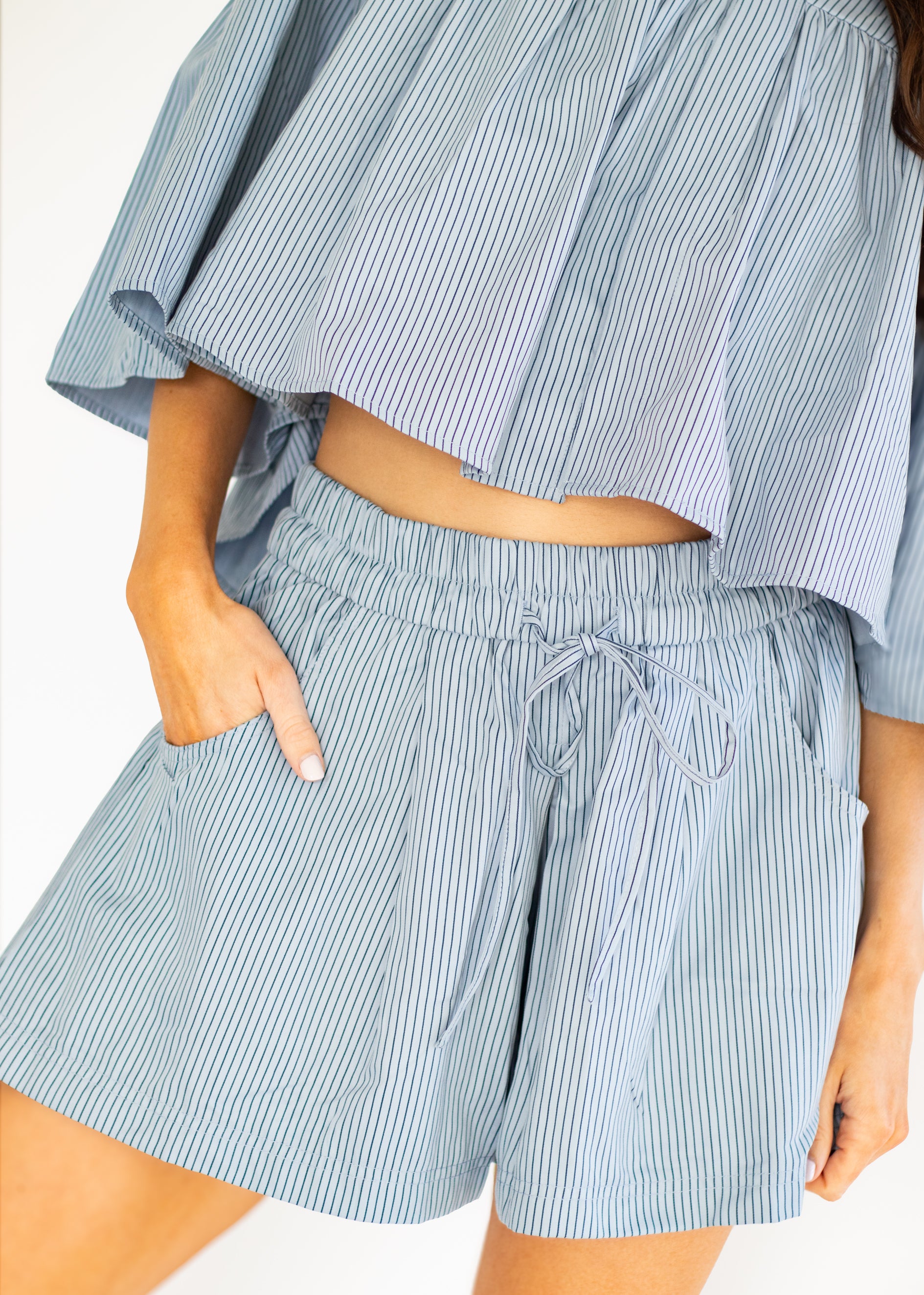 A close-up of a person wearing light blue and white vertically striped shorts with a drawstring waistband and a matching striped off-the-shoulder crop top.