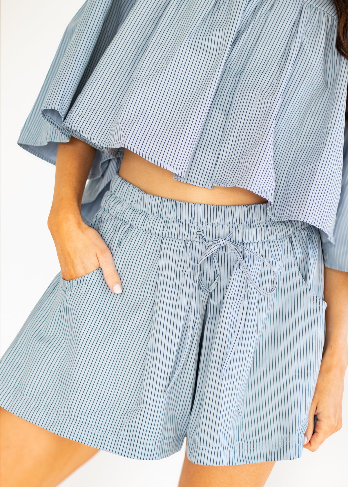 A close-up of a person wearing light blue and white vertically striped shorts with a drawstring waistband and a matching striped off-the-shoulder crop top.
