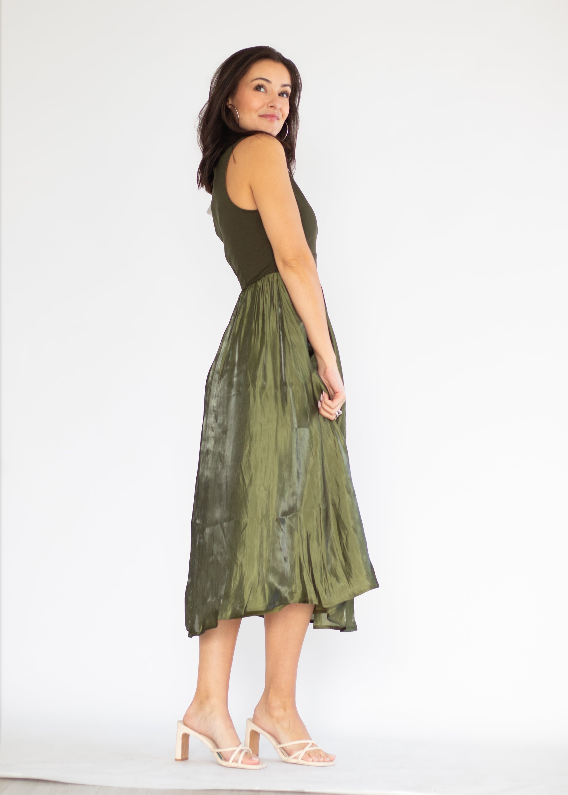 A woman modeling a sleeveless olive green dress with a fitted bodice and a flowing midi skirt, shown from the back against a plain white studio background.