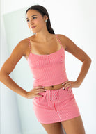 A woman modeling a red and white gingham two-piece set consisting of a spaghetti-strap crop top and matching high-waisted mini skirt, posed against a bright white background.