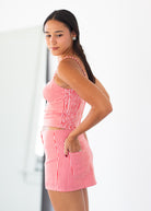 A woman modeling a red and white gingham two-piece set consisting of a sleeveless crop top and matching shorts, shown from a side-back angle against a bright white studio background.