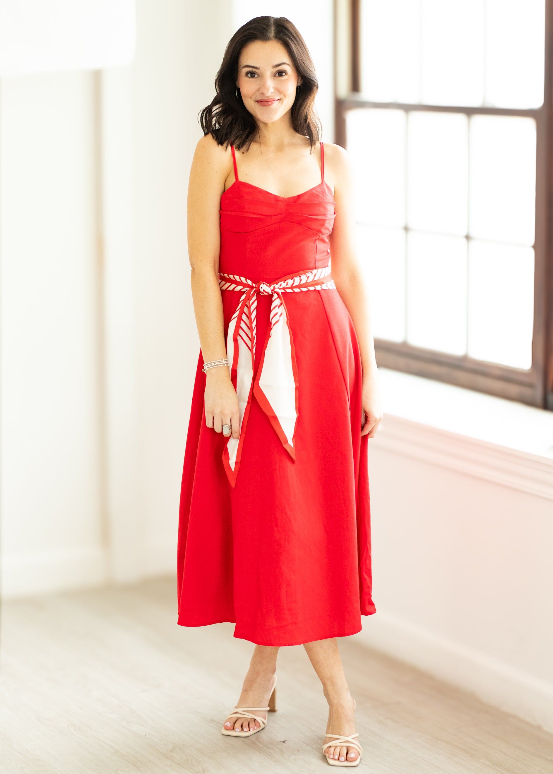 Woman wearing a red dress with a white belt on a beige background

