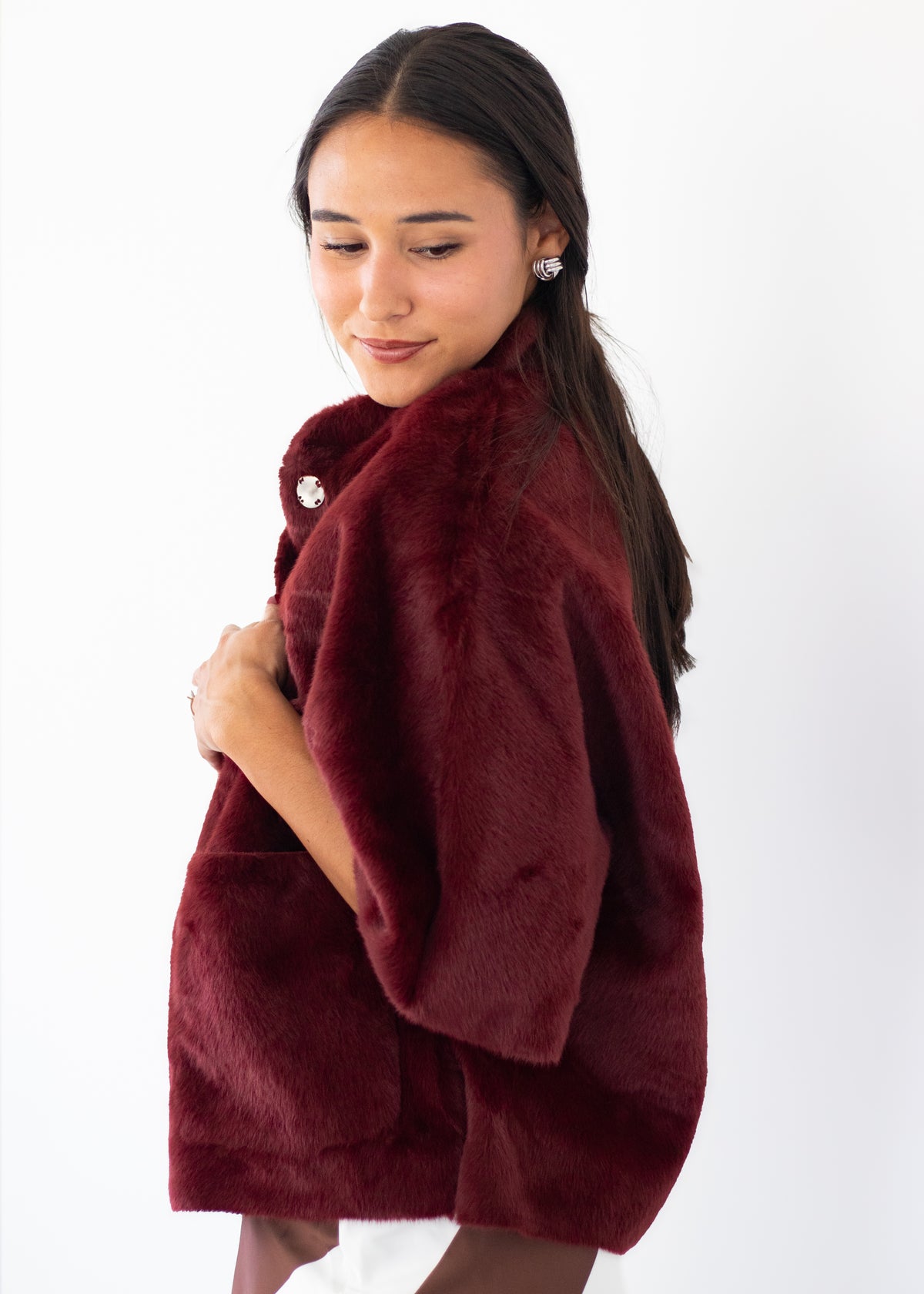 A woman wearing a plush, deep burgundy faux fur wrap or poncho with a decorative silver brooch, photographed against a clean white background.