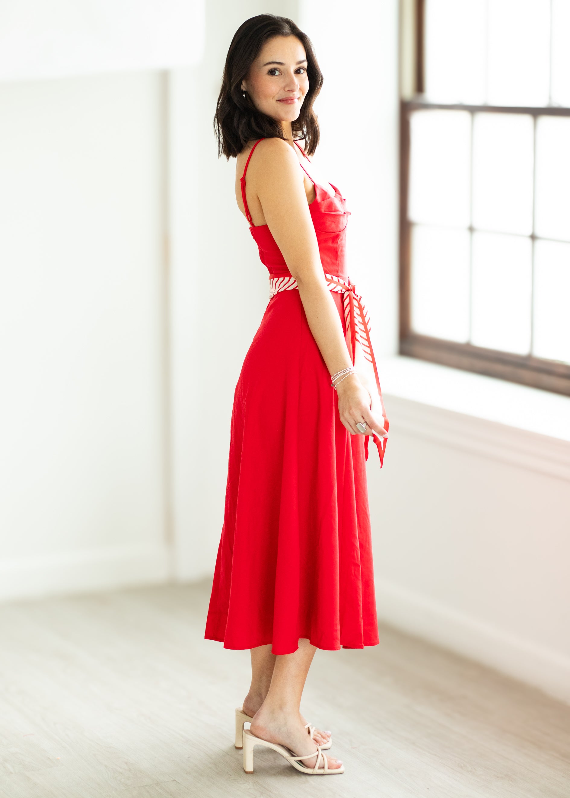 Woman wearing a red dress with a white belt on a beige background

