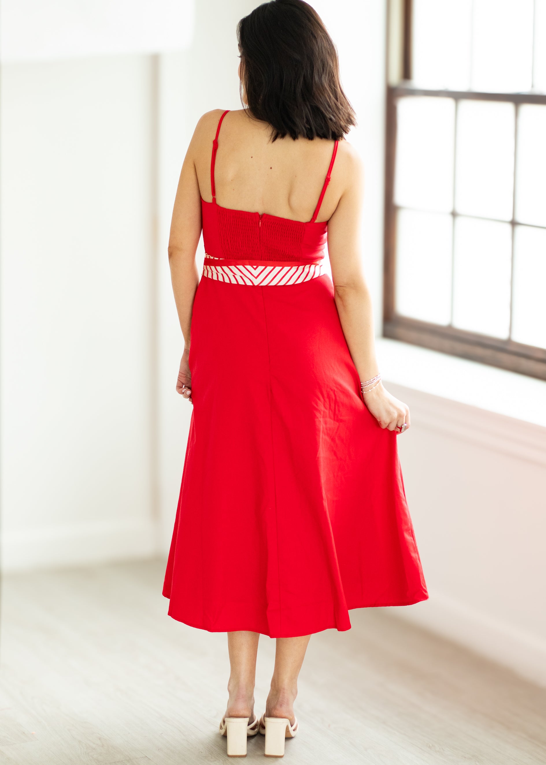 Woman wearing a red dress with a white belt on a beige background

