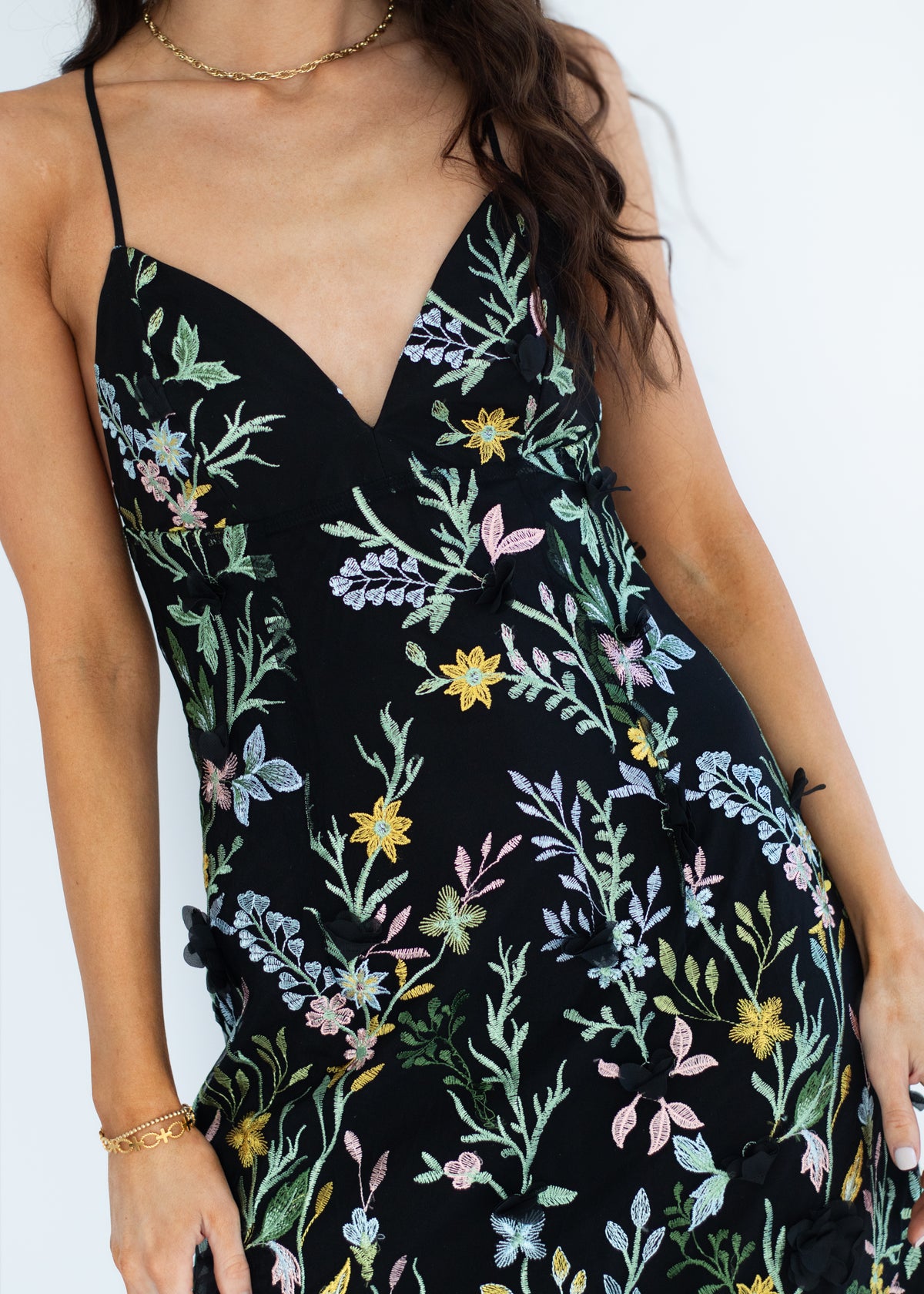 A close-up of a woman wearing a black spaghetti-strap dress with a colorful floral and butterfly print, featuring a V-neckline and side buttons.