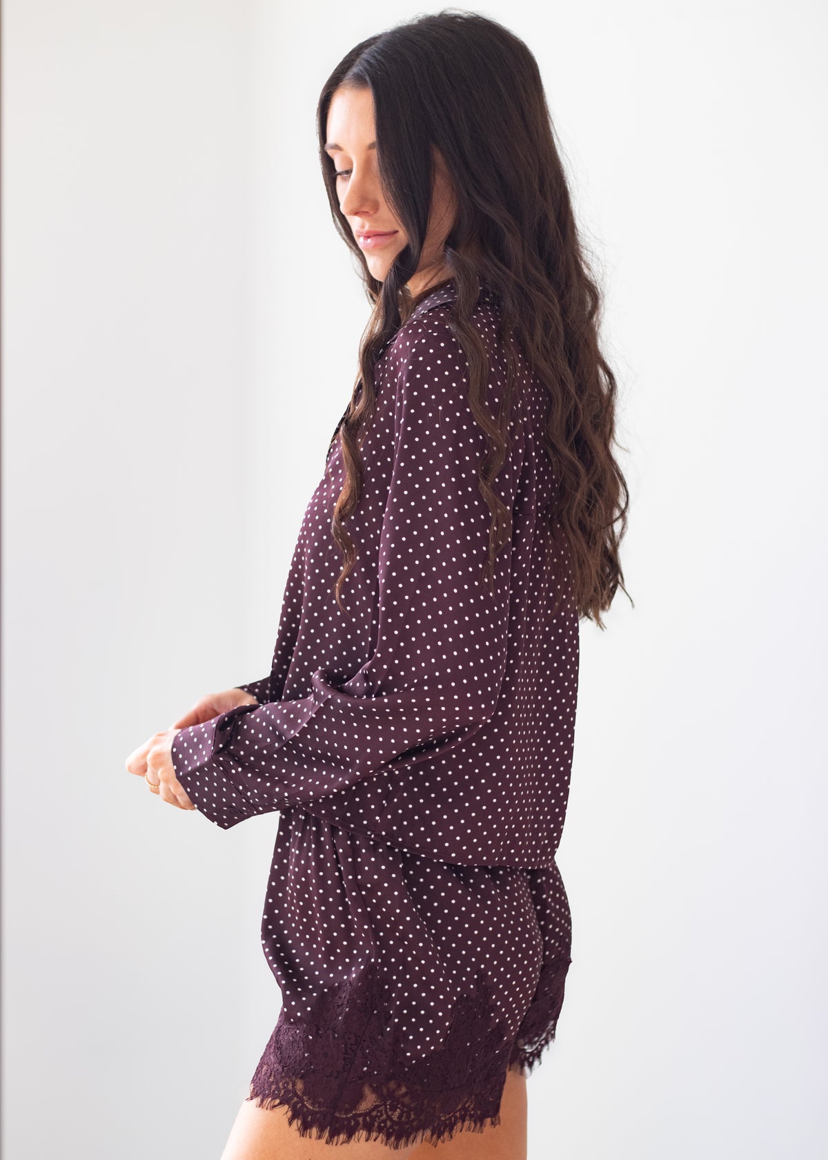 A woman wearing a dark plum purple long-sleeve top with white polka dots and a matching fringed skirt, shown from a side profile against a plain white background.