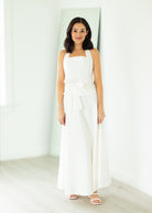 Woman wearing a white halter neck dress with a belt on a beige background

